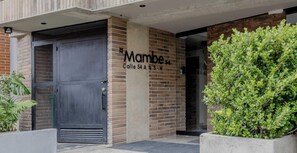 L'ingresso di un edificio con un cancello nero, un cartello con la scritta 'Mambe' e un muro in mattoni.