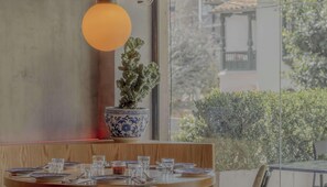 A dining area with a table set for two, a potted plant, and a large window with a view of greenery. - NOK Lovely 1 BR in Chapinero (Bogotá)