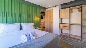 Habitació d'hotel moderna amb un llit, una paret decorativa de color verd, un armari de fusta i una cuinetta petita.