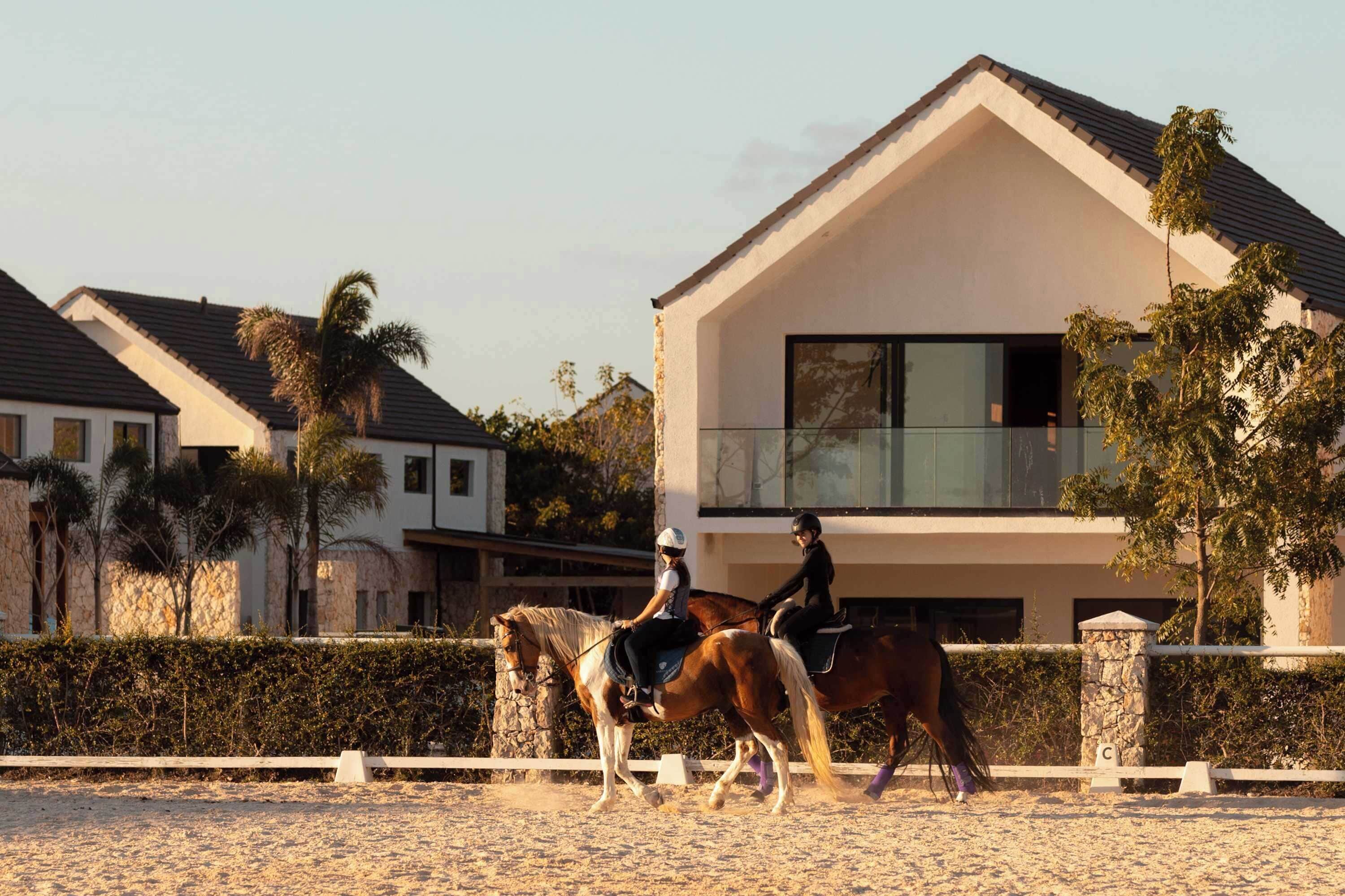 Una casa moderna con un balcón, un caballo y jinetes.