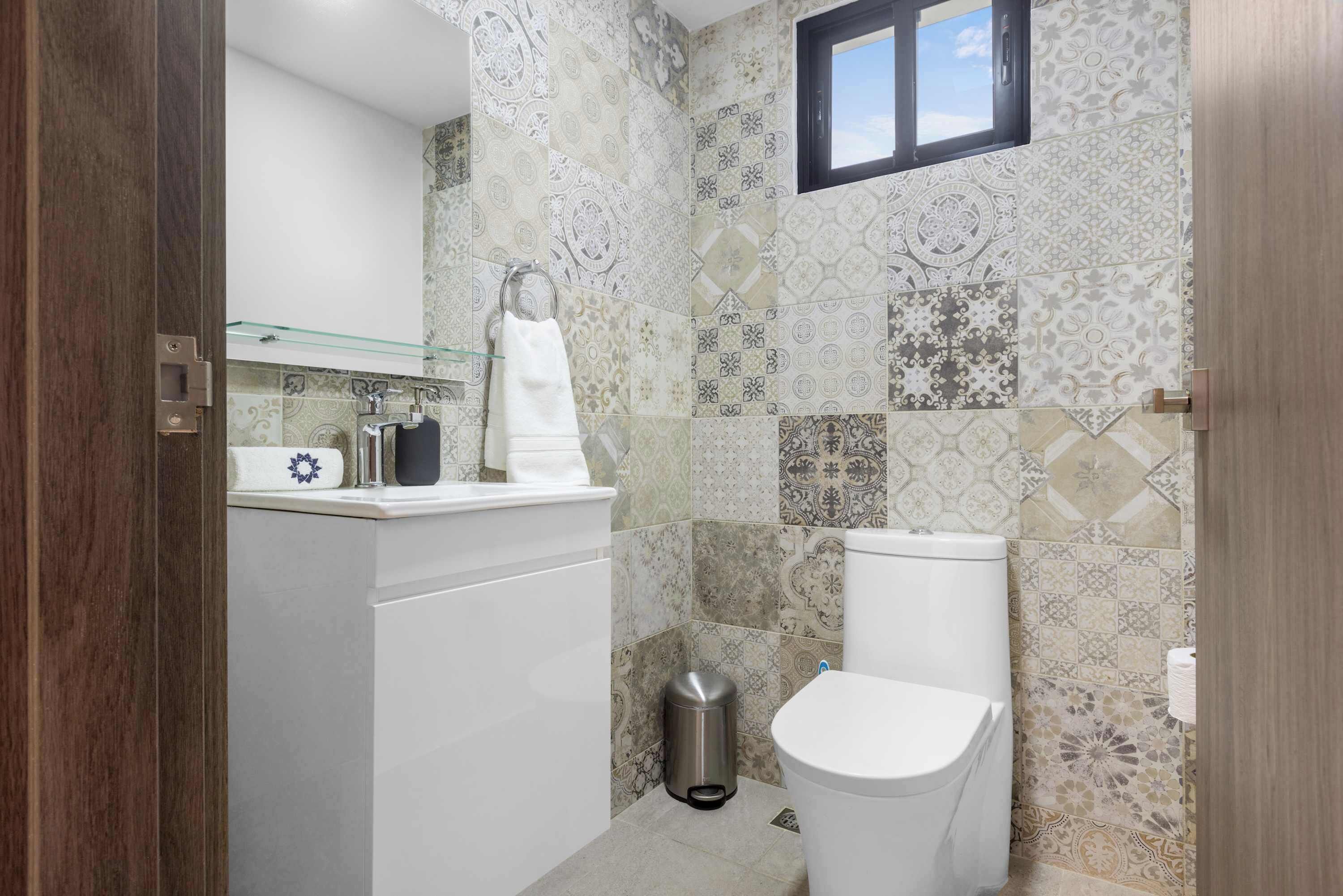 Ein Badezimmer mit Toilette, einer Glasablage und Fliesen mit Muster.