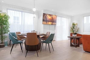 Ein modernes Wohnzimmer mit Essbereich, mit einem runden Tisch, sesseln in Türkis und Braun, einem großen Gemälde und einer Topfpflanze.
