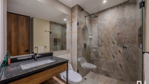 Um banheiro moderno com chuveiro de mármore, pia com toucador de madeira e vaso sanitário.