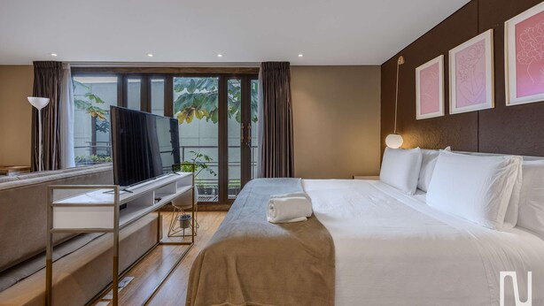 Quarto de hotel com cama, escrivaninha, televisão e varanda com plantas.