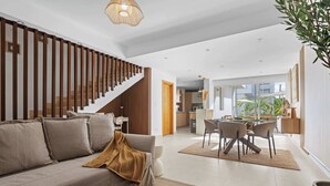 Ein modernes Wohnzimmer mit Sofa, Esstisch mit Stühlen, einer Treppe und einer Küchenzeile.