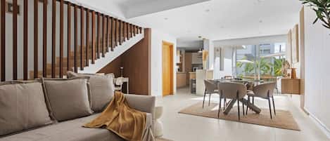 Una sala de estar moderna con un sofá, una mesa de comedor con sillas, una escalera y una zona de cocina.
