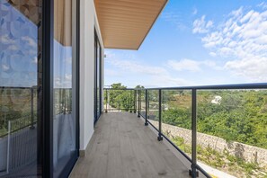 A balcony with a wooden floor and glass railings, overlooking a lush green landscape and a clear blue sky. - NOK Cozy 1BR Apartment the Towers By Vistacana (Punta Cana)
