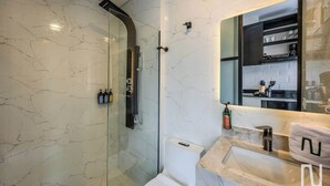 A modern bathroom with a glass-enclosed shower, a white toilet, and a marble sink with a towel. - NOK Designer Studio in Chico (Bogotá)