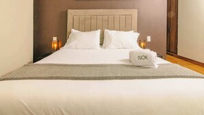 Een net opgemaakt bed met witte lakens, een beige hoofdbord en een kussen met 'niok' erop.