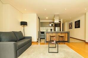 A modern living room with a sofa, a small table, and a kitchen in the background. - NOK Cozy 2 Br apt in Candelaria (Bogotá)