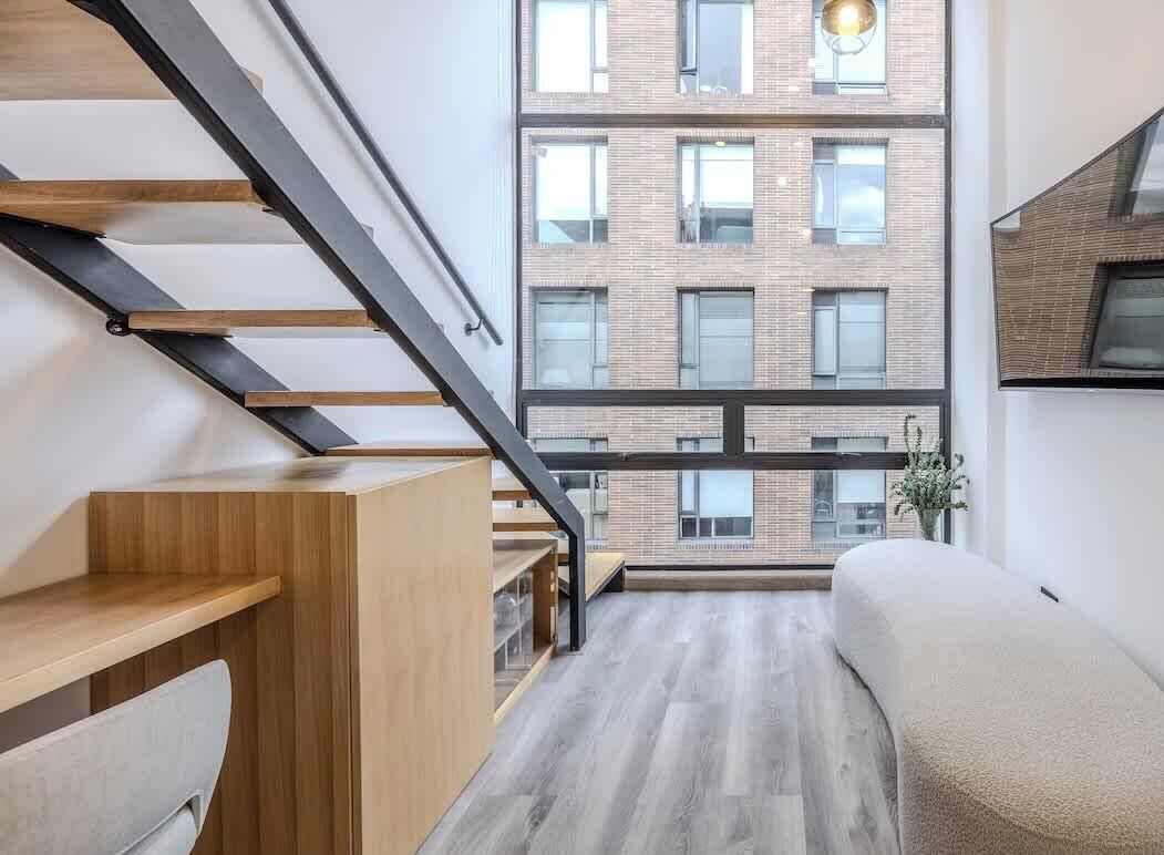 A modern interior with a staircase, a sofa, and a view of a brick building.
