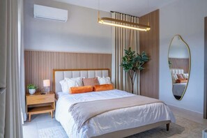 A bedroom with a bed, bedside table, lamp, mirror, and a potted plant. - NOK Classy 3BR Villa by Vistacana Rentals (Punta Cana)