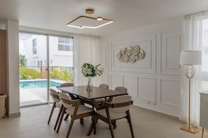 Uma área de refeições com mesa, cadeiras, um vaso com flores, uma luminária moderna e vista para uma piscina.