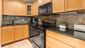 A kitchen with wooden cabinets, a black stove, a microwave, and a coffee maker. - Beachside Ground Floor Walkout. Heated Pool. BBQ Grills ☀️ (Cocoa Beach)