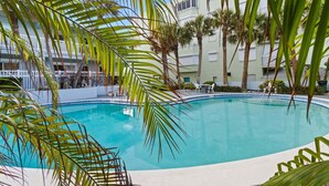 A swimming pool surrounded by palm trees and a white building with a balcony. - Beachside Ground Floor Walkout. Heated Pool. BBQ Grills ☀️ (Cocoa Beach)