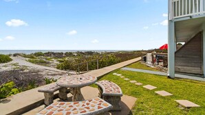 A patio with a mosaic table and benches, a wooden deck, and a view of the beach. - Beachside Ground Floor Walkout. Heated Pool. BBQ Grills ☀️ (Cocoa Beach)