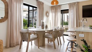Uma área de jantar moderna com mesa redonda, cadeiras de vime e uma ilha de cozinha com pia.