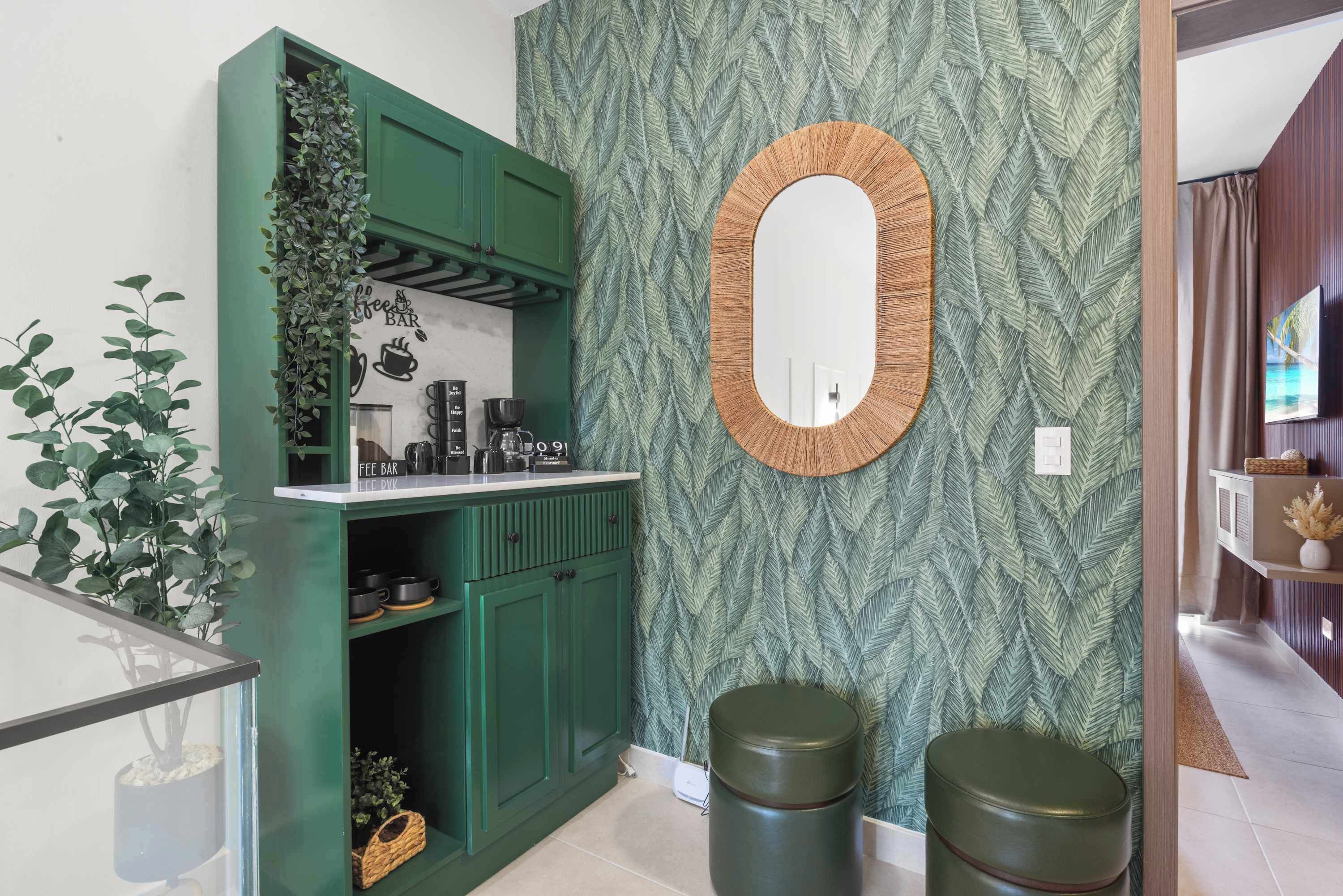 Una kitchenette con gabinetes verdes, una planta colgante, una cafetera y un espejo en la pared.