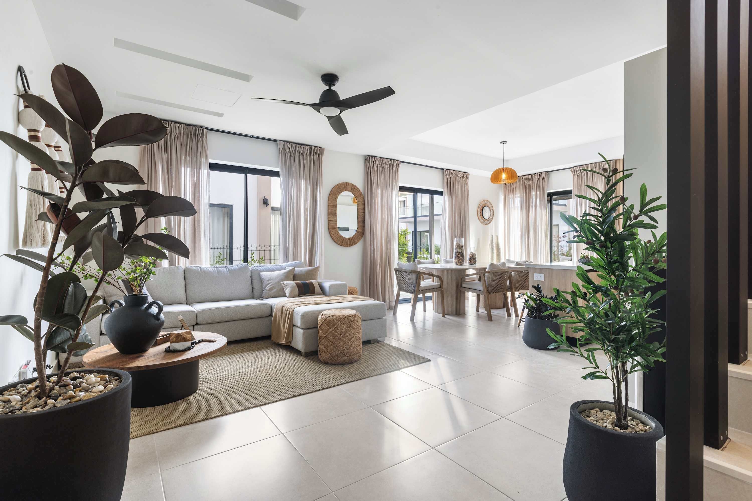 A modern living room with a sofa, coffee table, and potted plants. There is a dining area with a table and chairs.