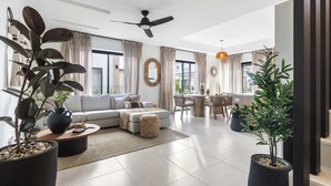 Uma sala de estar moderna com sofá, mesa de centro e plantas em vasos. Há também uma área de jantar com mesa e cadeiras.