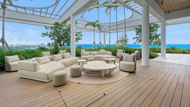 Een overdekte lounge buiten met een houten terras, witte meubels en uitzicht op de oceaan.