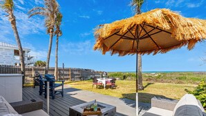Una terraza con mobiliario exterior, una sombrilla de paja y vista a la playa.