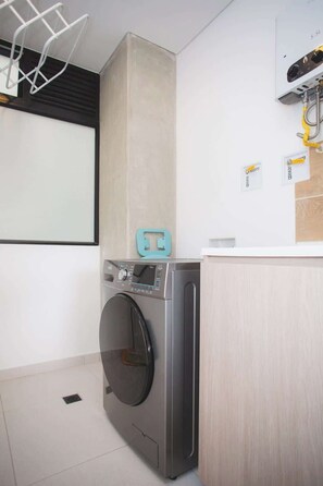 A compact laundry room with a front-loading washing machine, a drying rack, and a small cabinet. - NOK Amazing w/ Balcony 3 BR in Laureles Medellín (Medellín)