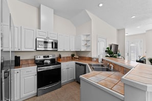 Eine moderne Küche mit weißen Schränken, einem eingebauten Backofen, einer Mikrowelle und einem Geschirrspüler sowie einer gefliesten Spritzschutzwand.
