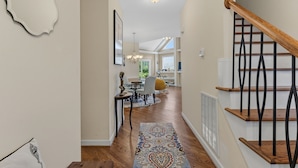 A hallway with a staircase, wooden flooring, a patterned rug, and a dining area with a table and chairs. - Modern Lakeview Escape: 2BR Golfers’ Retreat (Raleigh)