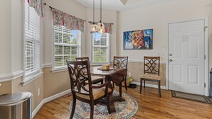 A dining area with a round table, four chairs, a chandelier, and a painting on the wall. - Modern Lakeview Escape: 2BR Golfers’ Retreat (Raleigh)