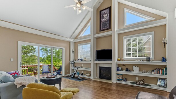 A spacious living room with a fireplace, large windows, and a ceiling fan. - Modern Lakeview Escape: 2BR Golfers’ Retreat (Raleigh)