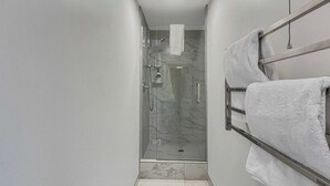 Ein modernes Badezimmer mit einer Duschkabine aus Glas, einem Handtuchhalter mit mehreren Handtüchern und einem Marmorboden.