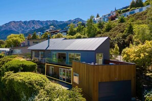 Een modern huis met een ruime glazen balkon, omgeven door weelderige begroeiing en bergen op de achtergrond.