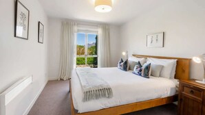 Ein Schlafzimmer mit einem großen Bett, einem Nachttisch, Vorhängen an einem Fenster und gerahmten Kunstwerken an den Wänden.