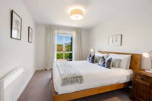 Een slaapkamer met een groot bed, een nachtkastje, een raam met gordijnen, en ingekaderde kunst aan de wanden.