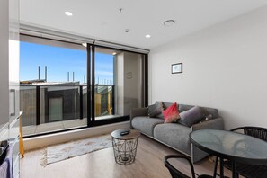 A modern living room with a sofa, a round table, and a large sliding glass door leading to an outdoor balcony. - The Union & Co Suite — Two Bedrooms, Two Bathrooms (Auckland City)