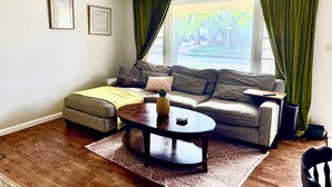 Ein Wohnzimmer mit einer Couch, einem Couchtisch, einem gemusterten Teppich und einem Fenster mit Vorhängen.