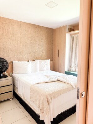 Ein Schlafzimmer mit einem Bett, einem Nachttisch, einem Ventilator und einem Vorhang.