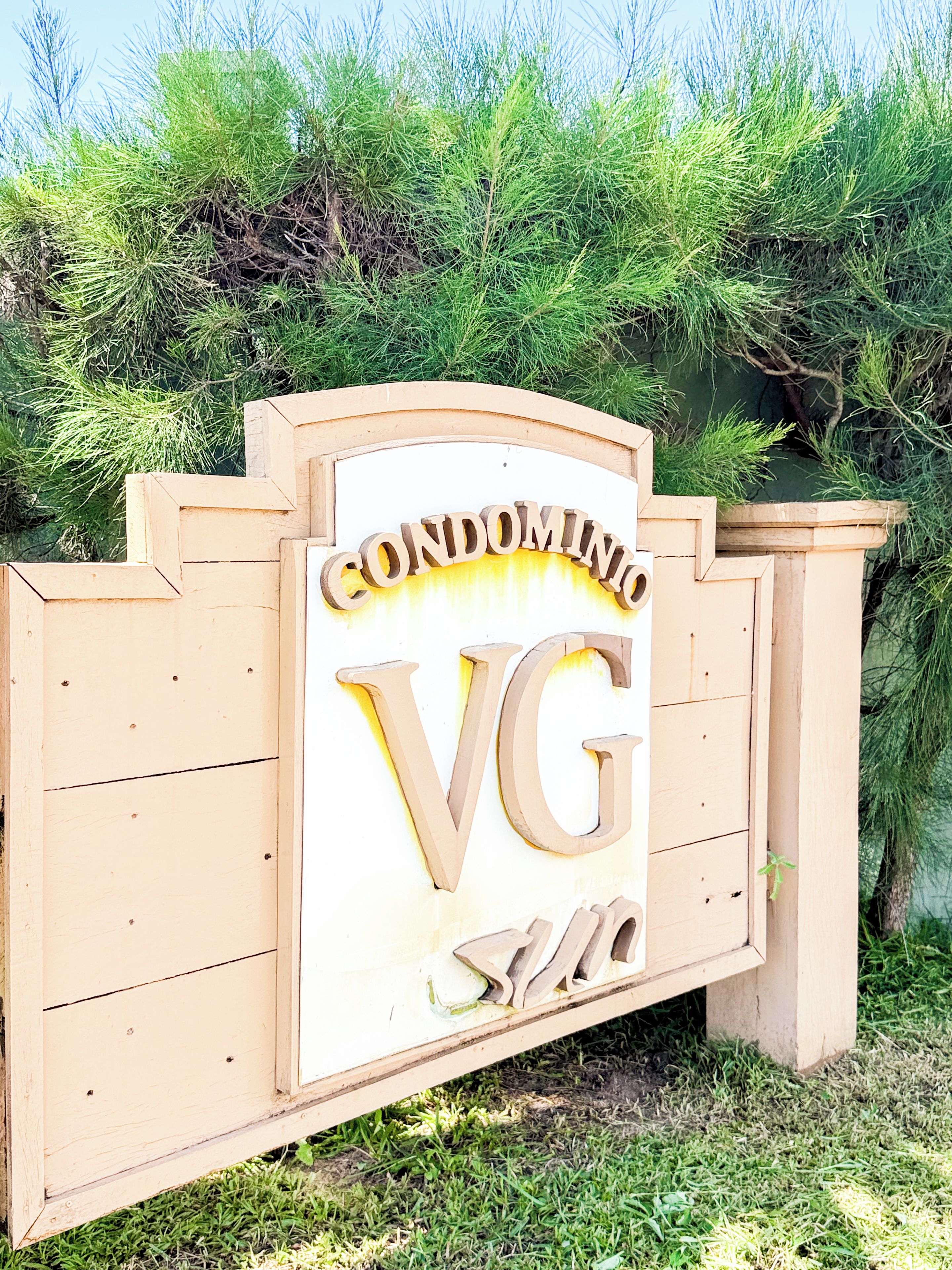 Ein Holzschild mit der Aufschrift 'CONDOMINIO VG', das ein Apartmenthaus kennzeichnet.