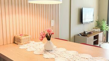 A dining area with a wooden table, a white vase with flowers, a lace table runner, and a hanging pendant light.