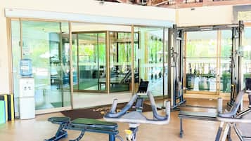 A gym with exercise equipment, glass doors leading outside, and a wooden ceiling structure.