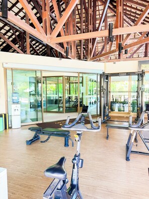 Uma academia com equipamentos de exercícios, portas de vidro que dão para o exterior e estrutura de teto em madeira.