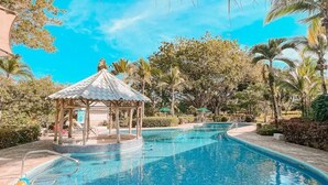 Une piscine d’un bleu éclatant, agrémentée d’un belvédère, entourée de palmiers et de chemins de pierre.