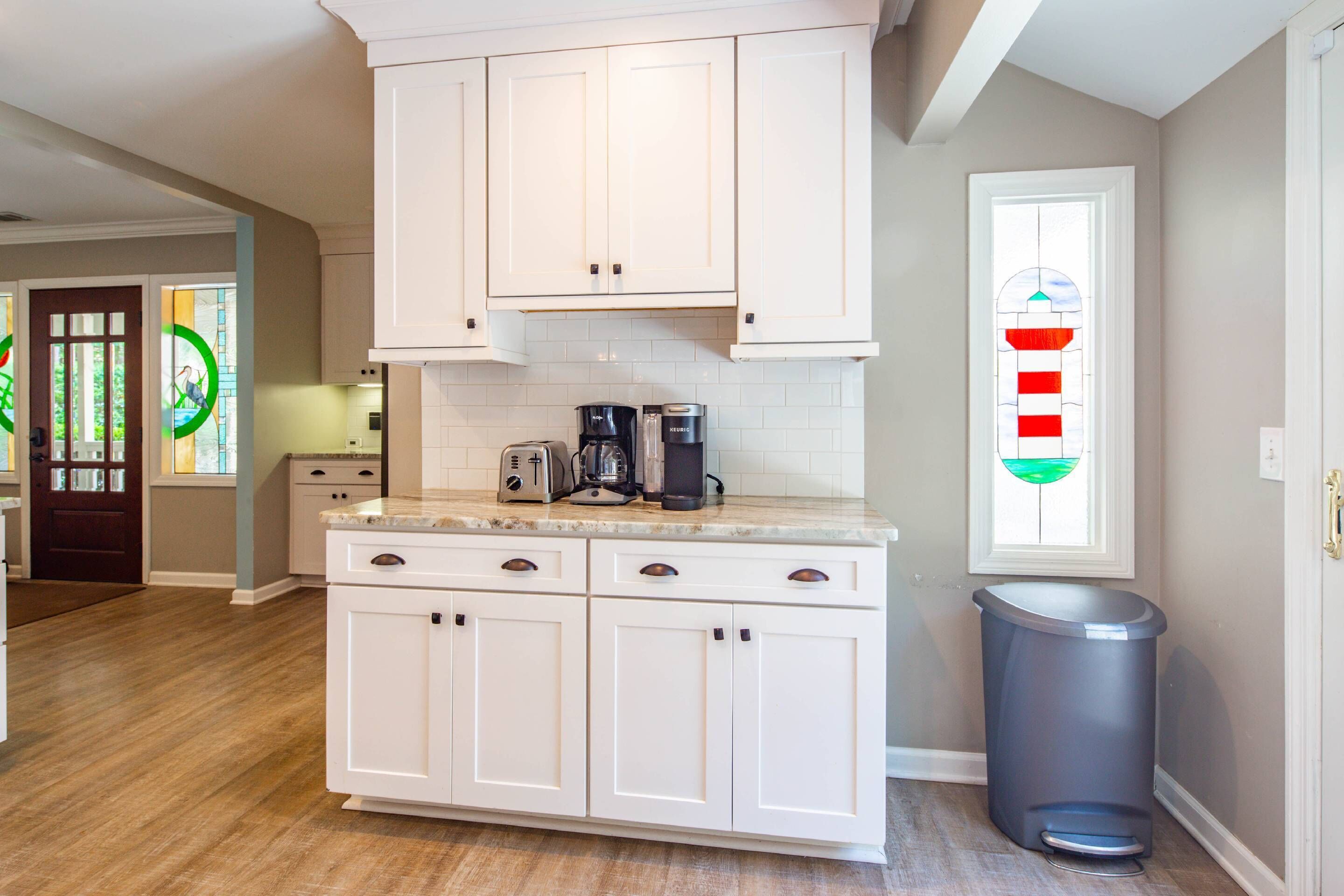 A kitchen with white cabinets, a countertop, a coffee maker, and a trash can.