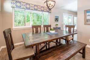 A dining area with a wooden table, four chairs, a bench, and a chandelier. - Bamboo-Lined Back Deck & Patio w/ Fire Pit; Dog-Friendly; Community Pool, Pickleball & Playground (Hilton Head Island)