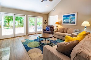A living room with a sofa, armchair, coffee table, and a painting on the wall. - Bamboo-Lined Back Deck & Patio w/ Fire Pit; Dog-Friendly; Community Pool, Pickleball & Playground (Hilton Head Island)