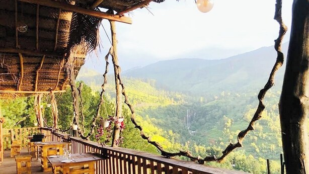 Una terraza de madera con bancos y una mesa, con vistas a un paisaje montañoso.