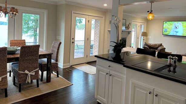 A modern kitchen with white cabinetry, a black countertop, and a dining area with wicker chairs. - Lake Murray home with boat ramp, dock, panoramic views close to USC@Columbia. (Chapin)