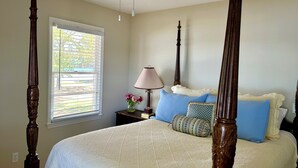 A bedroom with a four-poster bed, a ceiling fan, a window with blinds, a bedside table with a lamp, and decorative pillows. - Lake Murray home with boat ramp, dock, panoramic views close to USC@Columbia. (Chapin)