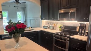 Une cuisine moderne avec des meubles de couleur sombre, des appareils électroménagers en acier inoxydable, un îlot central agrémenté d’un vase de fleurs et une vue sur le côté gauche.